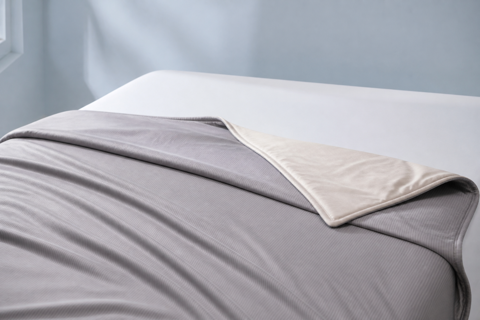 Two-sided gray cooling comforter draped on a bed